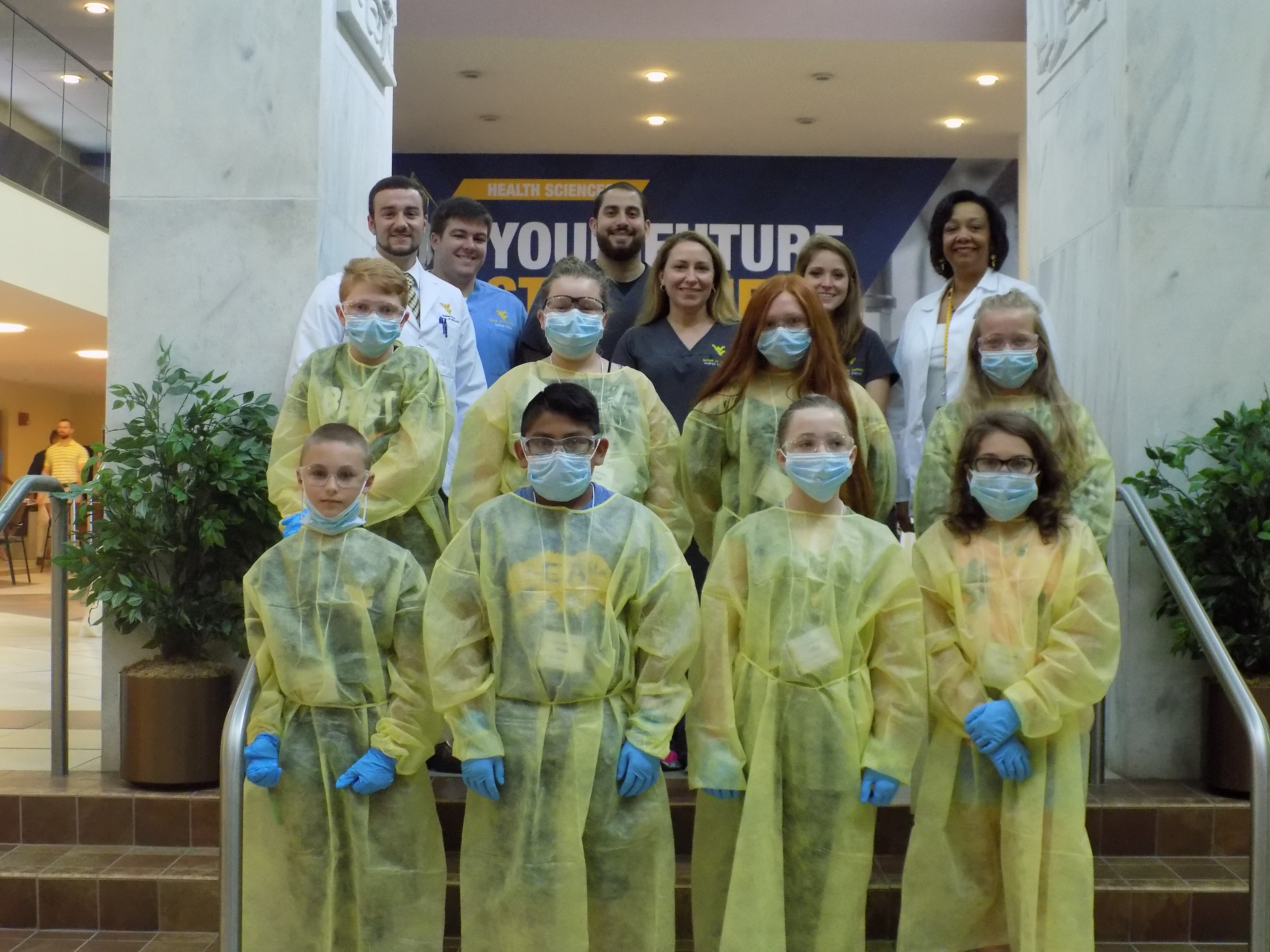 Brush with Dentistry participants pose with students and faculty wearing protective gowns, gloves and masks.